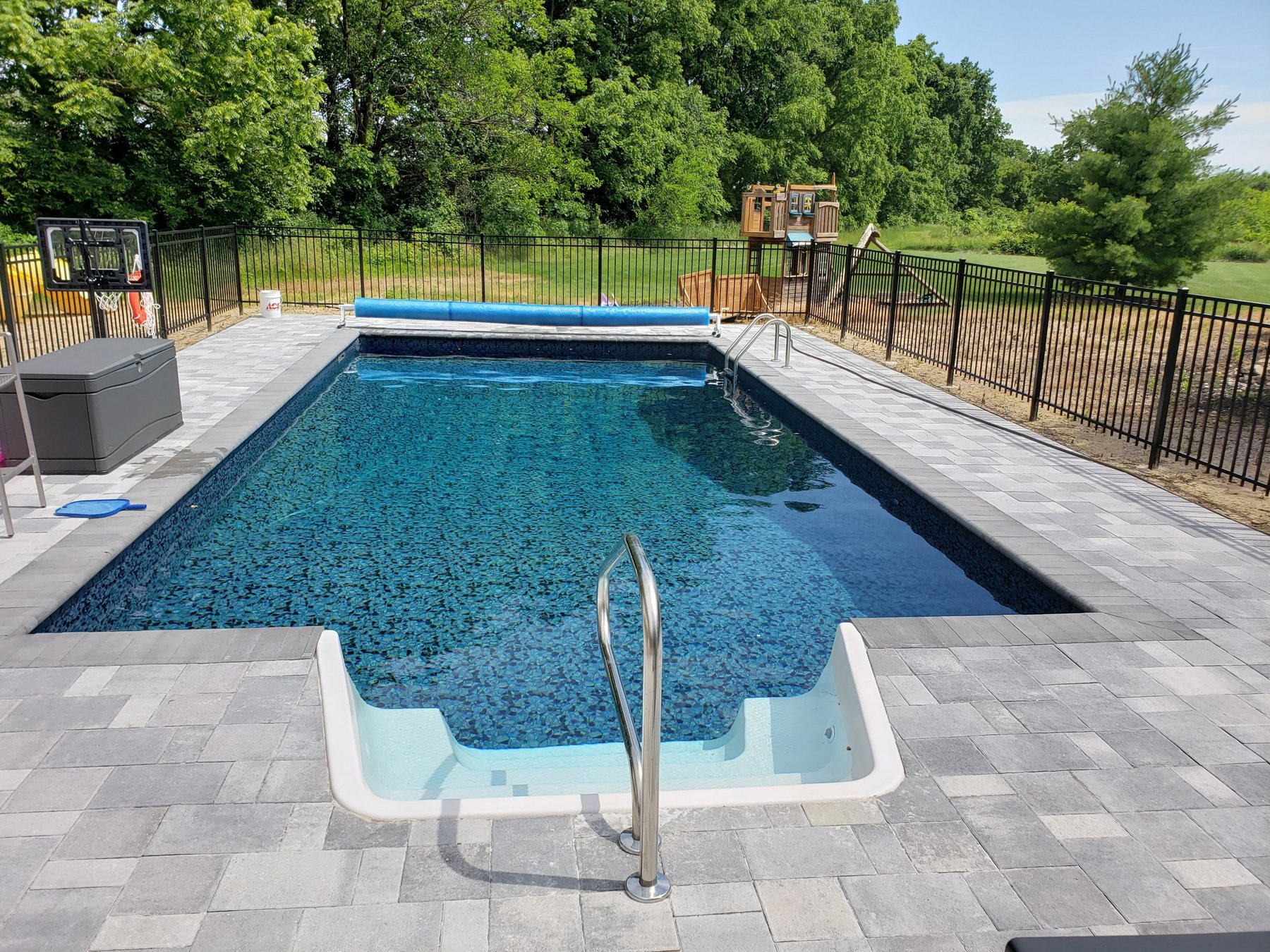 Completed curved backyard pool with stone deck by Blue Water Pools of Michigan